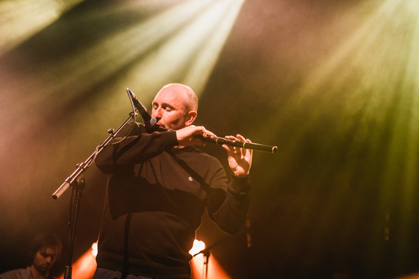 Image of Michael McGoldrick performing live. He is playing the flute with stage lights shining down on him.