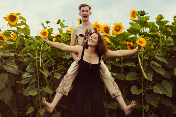 Bonnie is giving Pete a piggyback in a sunflower field. They both have big smiles.