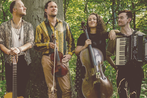 Good Trouble image. 4 musicians are stood posing with their instruments with a forest in the background. 