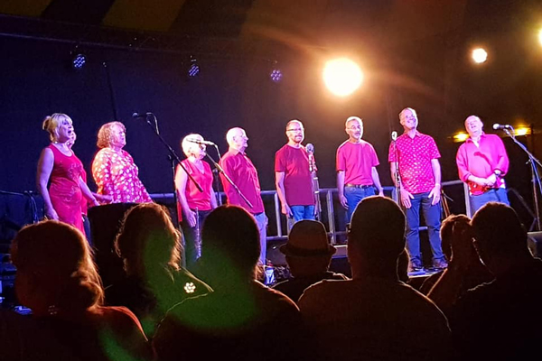 9 performers on stage in different red tops. 