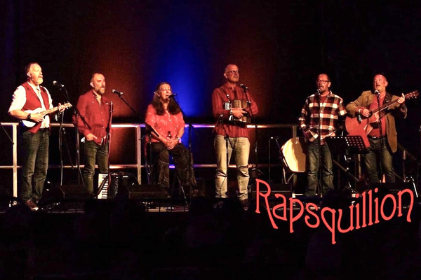 Rapsquillion image. Several members are onstage all with different types of red tops on. 