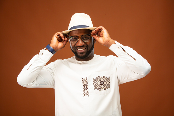 Seckou Keita image. Seckou is wearing a white top and white fedora style hat. this is a promotional photo shot with an orange background.