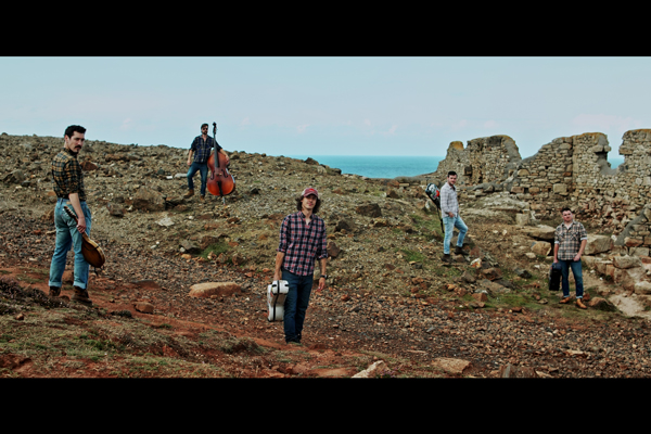 Flats & Sharps image. </p>
<p>The 5 band members are stood outside with their instruments with the backdrop of an old ruin and the sea. 