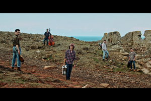 Flats & Sharps image. </p>
<p>The 5 band members are stood outside with their instruments with the backdrop of an old ruin and the sea.
