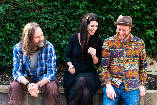 The Lost Trades image. </p>
<p>The trio are sat outside on a wall in front of a green leafy background. They are smiling and laughing. 