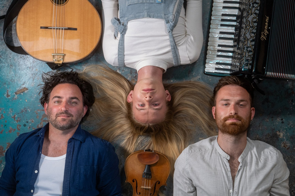 Tarren image. The trio are laying on the floor and we are looking from above. Next to each of their heads are their instruments. 
