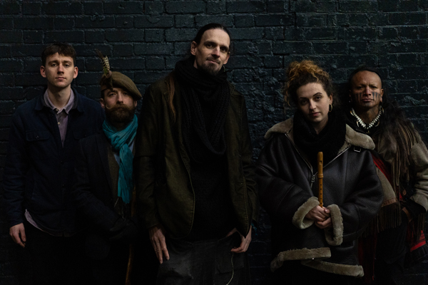 PerKelt image. </p>
<p>The 5 piece are stood in front a black brick wall. They are dimly lit wearing dark wintery clothes.