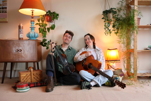 Tóchar image. The duo are sat on the floor with their instruments 